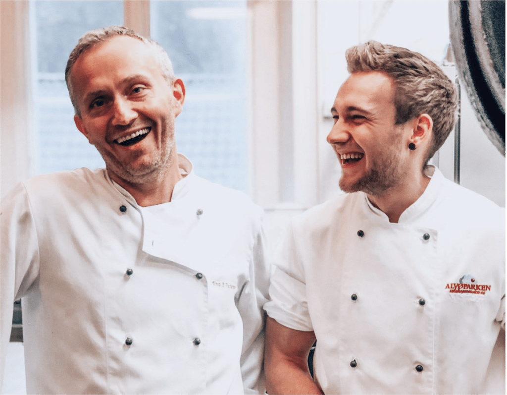 Two chefs happily share a laugh in a bustling kitchen, their smiles reflecting their passion for culinary artistry.